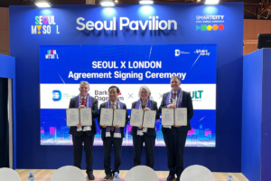 A photo of the four representatives from Barking and Dagenham, Connected Places Catapult, Thames Freeport and Seoul Digital Foundation holding their signed contracts on a podium titled Seoul Pavilion