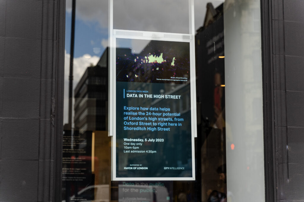 A digital screen with text talking about Data in the high street, viewed through a store-front window.