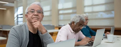Three elderly men using laptops at a table