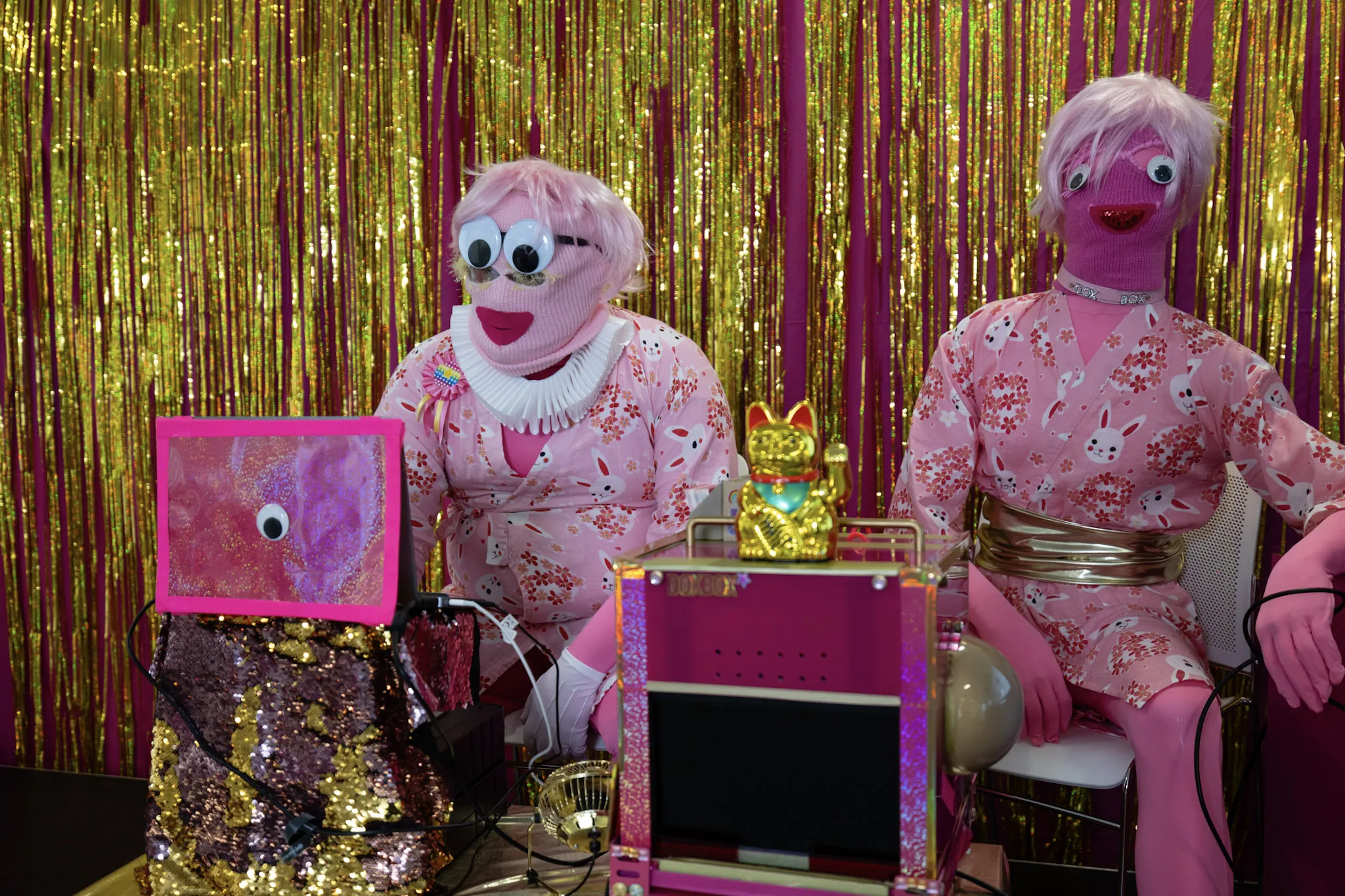 A picture of a performance of the Open Data Institute's 'DoxBox trustbot', with a mannekin and man in matching pink costumes sat around bright pink and gold furniture and backdrop. 