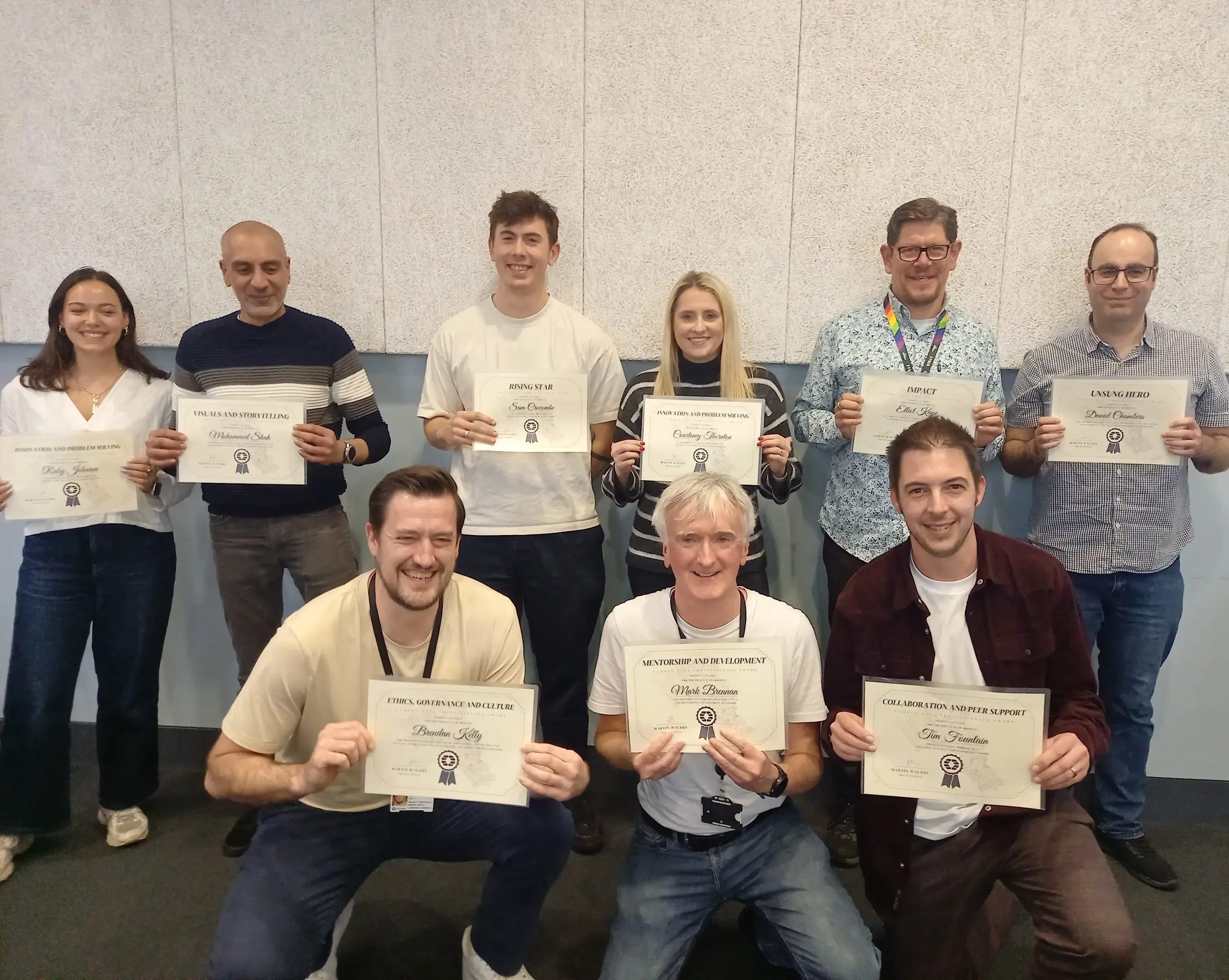 Several people smiling and holding their certificates in front of a decorated wall.
