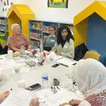 4 people sat around a table with leaflets on the table discussing