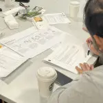 a person writing something on a piece of worksheet paper on a table, the table is shared with other people but they are not in the photo