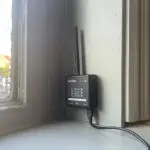 A photograph of a sensor attached to a wall by a window, the sensor is shaped like a black box with an antenna