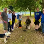 A photograph of seven individuals holding yellow bags in a park